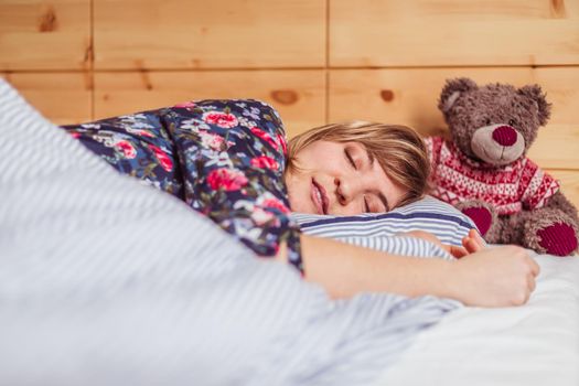 Young woman is sleeping peacefully with her teddy bear in her bedroom