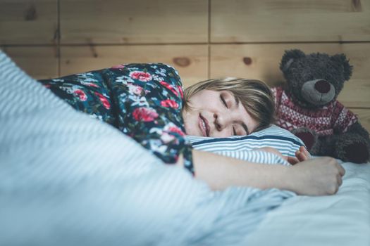 Young woman is sleeping peacefully with her teddy bear in her bedroom