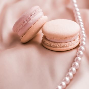 Girly, bakery and branding concept - Sweet macaroons and pearls jewellery on silk background, parisian chic jewelry, French dessert food and cake macaron for luxury confectionery brand, holiday gift