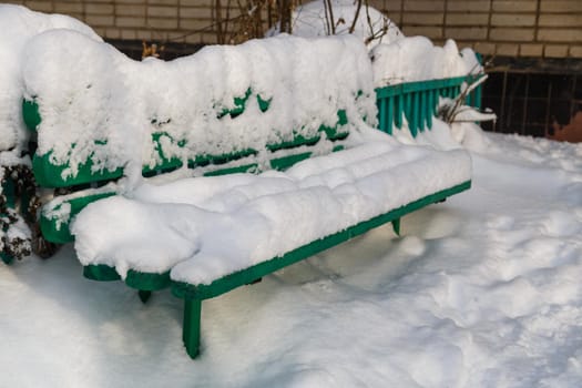 green bench near apartment building entrance covered with thick layer of snow at winter daylight.
