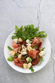 Salad arugula, Parma ham with sun-dried tomatoes, mozzarella slices, croutons, capers, seasoned oil and spices