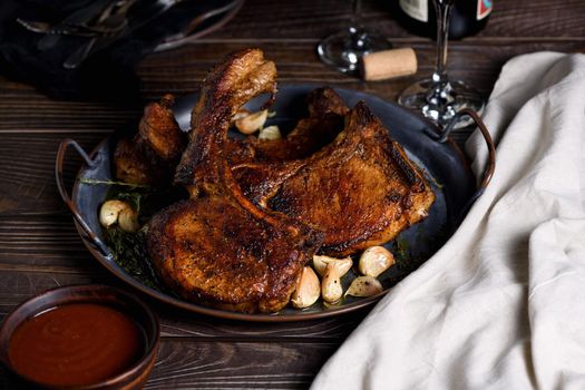 Juicy, slice of fried pork chop on a bone in oil with garlic and herbs in a pan. Close-up.