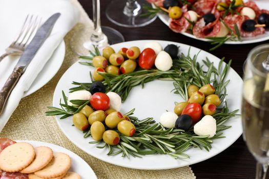 An appetizer of rosemary stuffed with olives with baby mozzarella and cherry tomatoes. Made in the form of a Christmas wreath.