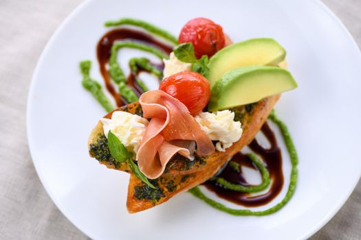 Toasted baguette toast with pesto sauce, a slice of Parma ham, mozzarella, tomato and avocado