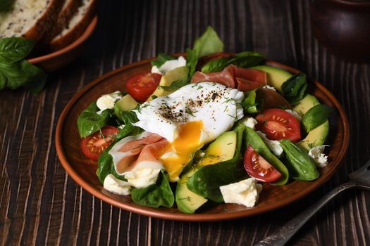 Eggs Benedict (Poached) with Parma ham, slices of avocado, tomato and tender spinach leaves, seasoned with flavored spicy olive oil