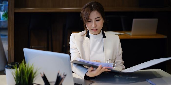 Joyful businesswoman sitting at desk looking at paperwork and talking with friend make informal video call