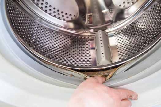 the hand protrudes the rubber band of the washing machine drum with a layer of dirt underneath.
