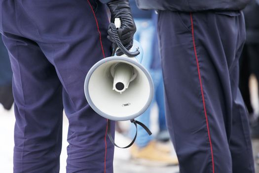 police officer holding loudspeaker megaphone at daylight, close-up with selective focus