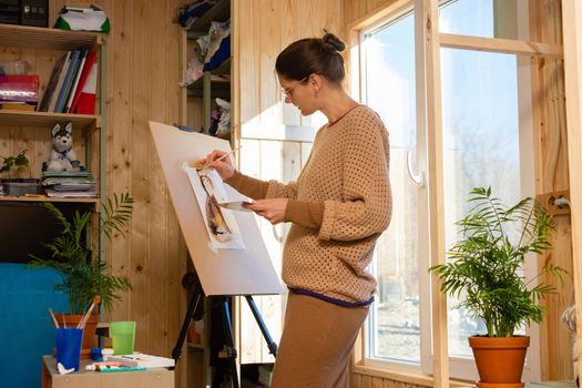 Girl artist draws on an easel at home, molubert stands at the window