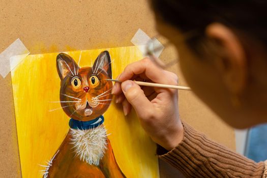 The artist draws with acrylic paints a drawing of a cat on an easel, close-up