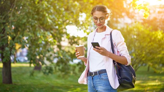 Businesswoman standing summer park Business person using smartphone Outdoors Successful european caucasian woman freelancer or teacher walking outside backpack dressed jeans white shirt pink jacket