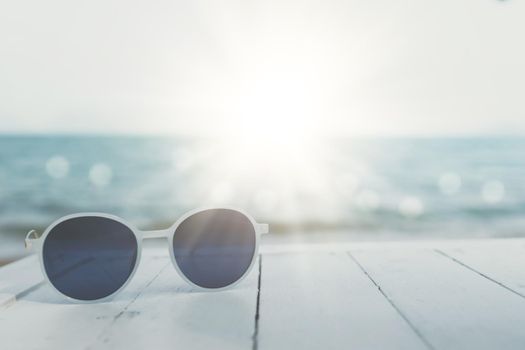 Selective focus of sunglasses on the table at summer beach resort with sunlight background. Holiday vacation travel tourism concept.