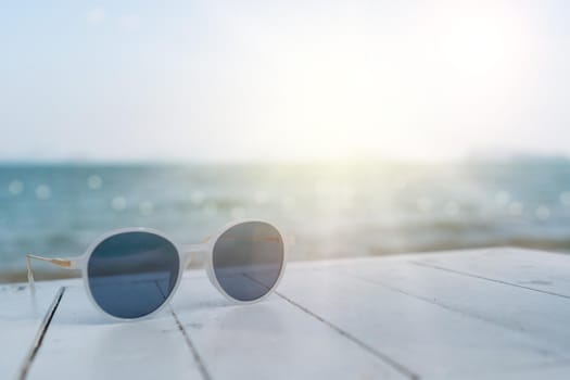 Selective focus of sunglasses on the table at summer beach resort with sunlight background. Holiday vacation travel tourism concept.