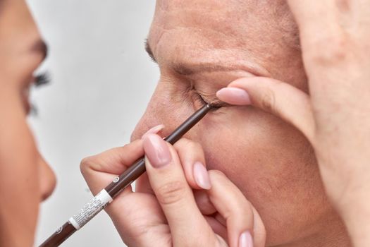 Woman at the reception at the beautician applies makeup. Master brings the eyebrows and eyelashes with a cosmetic pencil