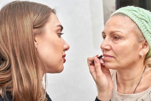 Woman at the reception at the beautician applies makeup. The master brings the lips with a cosmetic pencil