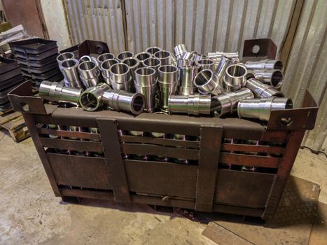 shiny steel cylindrical parts after turning operations overflowing big intermodal steel container box on factory floor