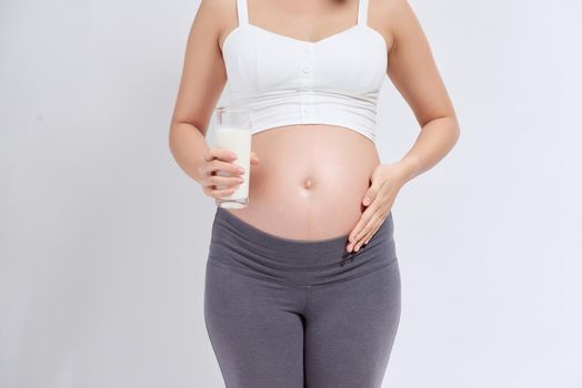 Happy pregnant woman drinking a glass of fresh milk and touching her belly 