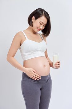 Happy pregnant woman drinking a glass of fresh milk and touching her belly 