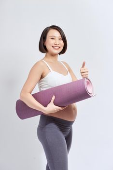 Young pregnant girl holding yoga mat and showing thumb up, lady wearing sporty clothing
