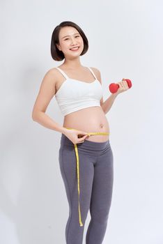 young pregnant woman doing fitness and measuring belly with measuring tape