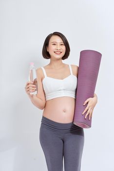 Active pregnant woman in sportswear holding exercising mat and bottle of water, empty space