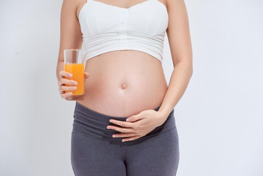 pregnant asian people standing on white room, she drinking fresh orange juice, she use her hand holding a glas