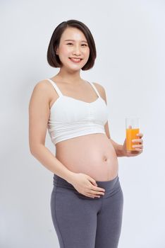 pregnant asian people standing on white room, she drinking fresh orange juice, she use her hand holding a glas