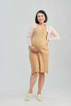 cheerful pregnant asian girl touching belly on white