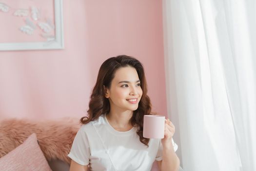 happy woman with coffee mug sitting on couch at home in apartment