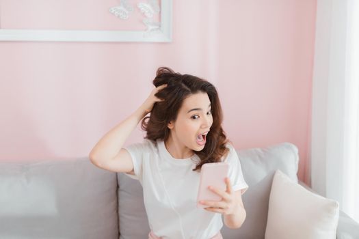 Angry woman screaming on the phone sitting on sofa in bright living room