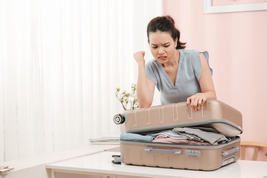 Low section of woman kneeling on overstuffed suitcase on bright room