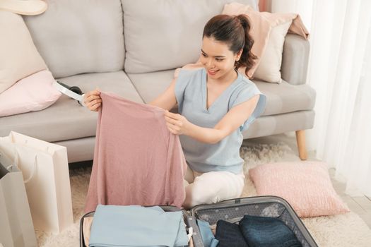 Young asian woman packing clothes into travel bag - Luggage and people concept