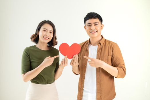 Beautiful young loving couple is holding a card in the shape of heart over white background.
