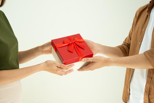 Close-up of man giving red gift box to woman over white background
