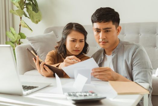 frowning young woman holding papers and looking at camera while using laptop with boyfriend at home