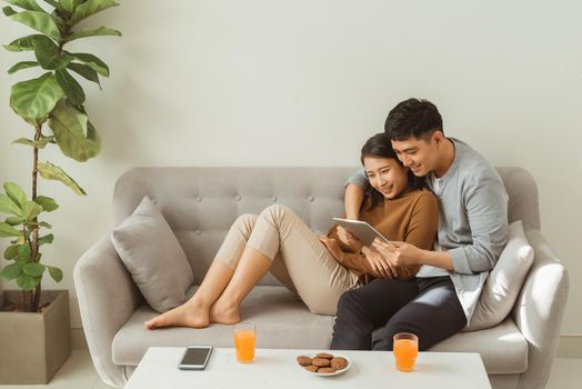 A young, attractive couple is seated together on a couch and are reading a tablet together.
