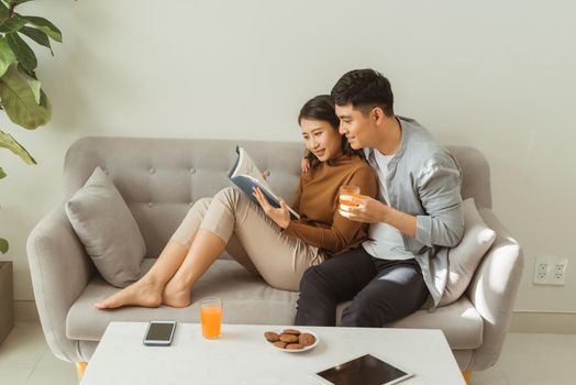 Portrait of young couple reading book sitting on couch