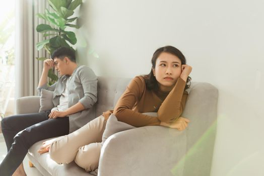 Upset couple at home. Handsome man and beautiful young woman are having quarrel. Sitting on sofa together. Family problems.