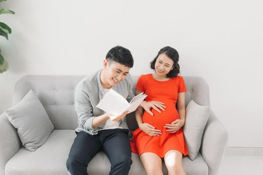 Close-up of a pregnant woman and her husband reading a book on the sofa at home