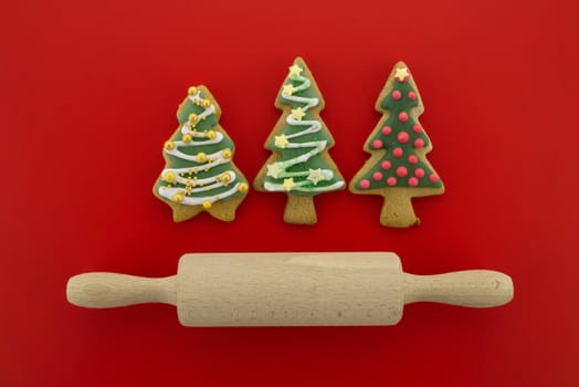 Christmas food and baking concept with a selection of colorful glazed or iced cookies with rolling pen over a festive red background in a flat lay still life