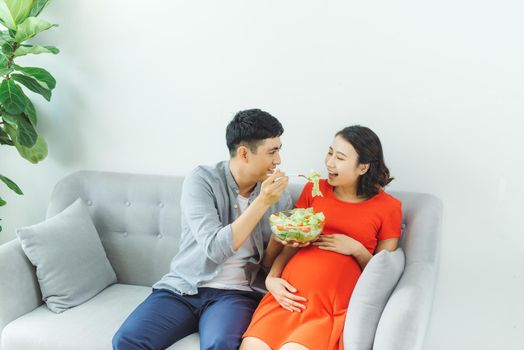 Happy young couple eating salad together at sofa in living room