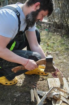 A bearded man in overalls chopping wood for a fire. Birch branches. Close-up.