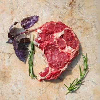 A fresh piece of beef with ribs, ready to roast. Nearby are the spices of rosemary. On a stone cutting board