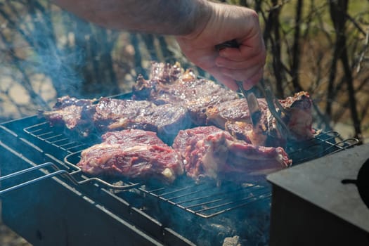 A man cooks meat on the grill, turning it over with tongs. Close-up