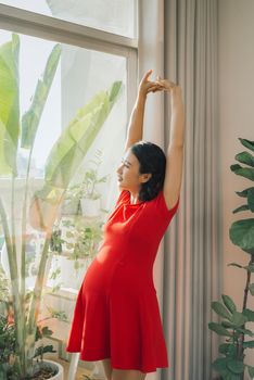 Beauty pregnant woman stretching her hand near the window