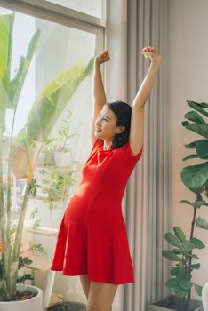 Beauty pregnant woman stretching her hand near the window