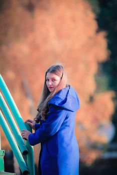 A young girl walks in the autumn park, stands behind a tree. The trees have yellow leaves.