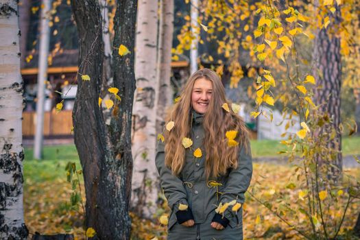 A young girl walks in the autumn park, stands behind a tree. The trees have yellow leaves.