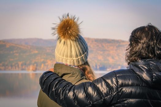 Young couple looks into the distance to the opposite shore of the lake in the autumn forest