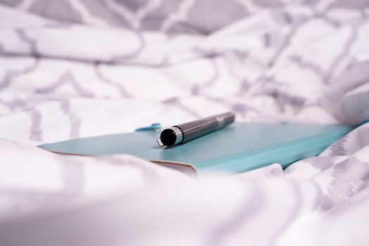 Close up of a notepad and pen on bed with modern bright bed sheets. Mobile working concept. Freelance, distance learning or work from home concept.